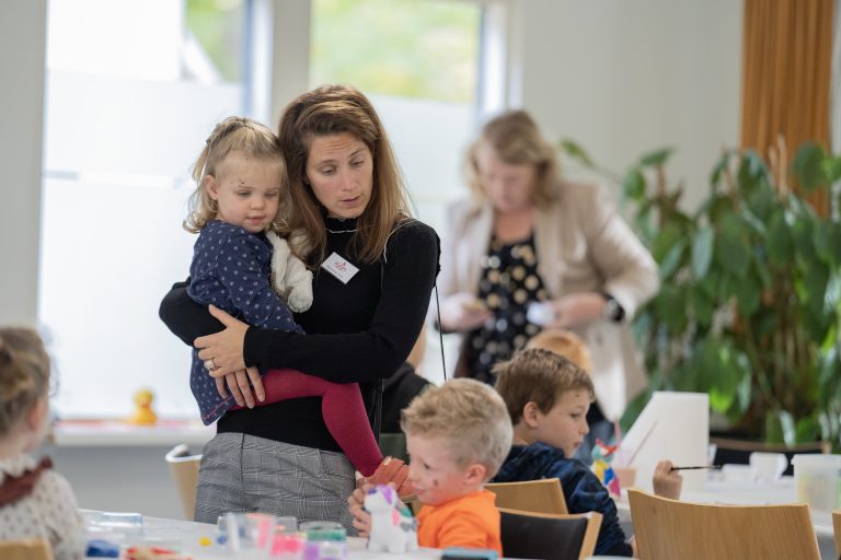 moeder-draagt-dochter-en-kijkt-naar-knutslende-kinderen_2023-11-04-11.42.10-6